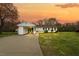 Charming single-story home featuring a connected carport, manicured lawn, and a welcoming front porch under an orange sunset sky at 118 Tysor Cir, Graham, NC 27253