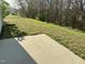 Concrete patio in a backyard with a grassy slope and tree line, partially shaded by a building at 3316 Perkins Ridge Rd, Raleigh, NC 27610