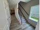 Carpeted staircase with dark metal balusters and wood handrail, alongside an open view of the kitchen and a bright window at 84 Commons Cir, Clayton, NC 27520