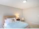 Well-lit bedroom featuring a comfortable bed with neutral bedding, a side table, and neutral walls at 8417 Henderson Rd, Apex, NC 27539