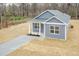 Aerial view of single-story home features gray siding, green roof, tidy landscaping, and a front porch with bare trees in background at 175 David Ln, Roxboro, NC 27573