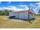 Metal shed with roll-up doors, a trailer, and gravel surroundings, set against a green lawn and trees at 5595 Godwin Lake Rd, Benson, NC 27504