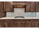 Close-up of a kitchen featuring a cooktop, dark wood cabinets, stylish backsplash, and granite countertops at 215 Mystic Pine Pl, Apex, NC 27539