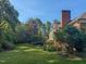 Expansive backyard with mature trees, lush greenery, and a glimpse of a brick home with a large chimney at 382 Wimbledon Dr, Roxboro, NC 27573