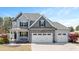 Charming two-story home with a three-car garage, stone accents, and a covered front porch, set against a blue sky at 14 E Saddle Ct, Archer Lodge, NC 27527