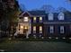 Charming brick home with a welcoming porch, illuminated by landscape lighting in the manicured front yard at dusk at 8508 Kayenta Ct, Wake Forest, NC 27587