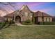 Charming stone and brick home with a beautiful yard and lush landscaping under a vibrant sunset sky at 915 Dunleigh Dr, Burlington, NC 27215