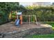 Backyard play area with a colorful playset and swings, surrounded by a retaining wall and lush greenery at 213 Billingrath Turn Ln, Cary, NC 27519