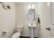 A half bathroom with a pedestal sink, toilet, oval mirror, and wooden floors at 6021 Watsonia Dr, Zebulon, NC 27597
