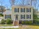 Charming yellow two-story home with black shutters, brick foundation, and mature trees in a well-maintained yard at 7109 River Birch Dr, Raleigh, NC 27613