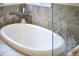 Close up of luxurious soaking tub with chrome fixtures and a tiled surround, with natural light from nearby window at 4303 Thetford Rd, Durham, NC 27707