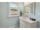 Bright bathroom with white vanity, framed mirror, and view of outdoor scenery through a window at 410 N Hyde Park Ave, Durham, NC 27703