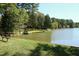 Picturesque lakeside view with mature trees and a grassy shoreline featuring a bench and picnic table at 5520 Mccormick Rd, Durham, NC 27713