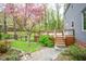 A wooden deck adjoins a gray home next to a yard with lush greenery and blooming pink trees at 5608 Ventura Dr, Durham, NC 27712