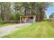 View of the shed from the driveway, surrounded by trees and green grass at 2603 Brogden Rd, Creedmoor, NC 27522