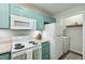 Bright kitchen featuring white appliances, blue-green cabinetry and view into laundry area at 3050 Trailwood Pines Ln # 101, Raleigh, NC 27603