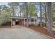View of exterior with gravel driveway, brick carport, covered porch and mature trees surrounding the home at 927 Ferncrest Dr, Durham, NC 27705