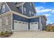 Attached two-car garage with white doors and stone and blue siding on a concrete driveway offers convenience at 1160 Duke Farm Dr, Wake Forest, NC 27587