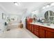 Bright bathroom features double vanity with cherry cabinets, tile backsplash and flooring, and a soaking tub under a window at 1312 Golden Bluff Ln, Fuquay Varina, NC 27526
