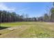 Spacious backyard with a wooded border, grass lawn, and a brick-lined area for a fire pit at 6480 Beaver Creek Rd, New Hill, NC 27562