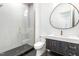 Modern bathroom featuring a glass shower, round mirror, dark vanity, and mosaic tile flooring at 1621 Bruce Circle, Raleigh, NC 27604
