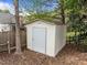 A white shed with a solid door sits in a yard surrounded by trees and a fence at 203 Grassy Point Rd, Apex, NC 27502