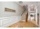 Hallway with hardwood floors and wainscoting, leading to a dining area and stairs with wooden banister at 8418 Wheatstone Ln, Raleigh, NC 27613