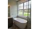 Soaking tub in bathroom with hardwood floors and a large window with backyard views at 5480 Thom Rd, Mebane, NC 27302