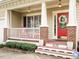 Inviting front porch with brick accents, white railings, and a vibrant red front door with seasonal wreath at 1625 Heritage Garden St, Wake Forest, NC 27587