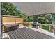 Covered deck featuring a hot tub, grill, wooden railing, and a view of the surrounding backyard trees at 2832 Steeple Run Dr, Wake Forest, NC 27587