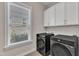Well-lit laundry room with modern washer and dryer, window, and overhead cabinets at 8121 Greys Landing Way, Raleigh, NC 27615
