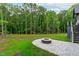 Stone fire pit is showcased on a patio surrounded by green grass and a lush wooded area in the backyard at 2200 Paddstowe Main Way, Wake Forest, NC 27587