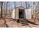 Sturdy exterior shed with a metal door and wooden steps, ideal for storage in a natural wooded setting at 4401 E L G Rd, Efland, NC 27243