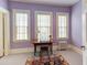 A bright bedroom featuring lavender colored walls, light carpet, three large windows and a wooden desk at 1208 College Pl, Raleigh, NC 27605
