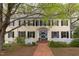 Two-story home showcasing yellow siding, black shutters, and a charming entryway framed by mature trees and landscaping at 1208 College Pl, Raleigh, NC 27605