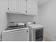 Bright laundry room features a side-by-side washer and dryer, tile floor, and custom white cabinets above at 2408 Merion Creek Dr, Apex, NC 27539