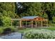 Outdoor pavilion with wooden beams, a stone patio, seating, and surrounding greenery at 817 Central Pk Dr, Raleigh, NC 27604