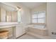A spa-like primary bathroom showing a large soaking tub, dual vanities, a decorative laundry basket, and soft lighting at 9201 Club Hill Dr, Raleigh, NC 27617