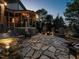 Illuminated outdoor stone patio boasts a built-in grill, dining area, and relaxing fire pit at twilight at 5768 Cavanaugh Dr, Raleigh, NC 27614