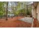 View of the backyard with a stone patio, mature trees, and pine straw ground cover at 120 Cypress View Way, Apex, NC 27502