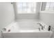 Brightly-lit bathroom featuring a luxurious white soaking tub beneath a patterned window at 1725 Langlais Dr, Graham, NC 27253