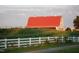 A picturesque red barn is nestled amidst lush greenery, framed by a white fence at 3308 Churchill Rd, Raleigh, NC 27607
