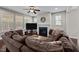 Inviting living room featuring a cozy fireplace, ceiling fan, large windows and a plush, oversized brown sectional sofa at 1840 Flint Valley Ln, Apex, NC 27502