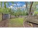 Green backyard featuring a wooden fence, stone firepit, green grass, shed, and a wood deck at 3 Maple St, Raleigh, NC 27610