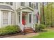 Inviting front porch with a red door, classic white railing, brick steps, and green landscaping at 5405 Whisperwood Dr, Durham, NC 27713