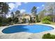 A sparkling pool with stone border and lush landscaping create a serene backyard oasis, with an elevated deck at 10001 Sandcreek Ct, Chapel Hill, NC 27517