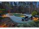 View of the lighted backyard pool with stone surround, mature trees, and lounge chairs at 10001 Sandcreek Ct, Chapel Hill, NC 27517