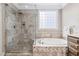Bright bathroom featuring a glass-enclosed shower, soaking tub, and travertine tile at 102 Kamprath Pl, Cary, NC 27519