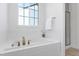 Modern bathroom featuring a soaking tub with chrome fixtures, tiled surround, and a window for natural light at 1165 Saint Cloud Loop, Apex, NC 27523