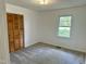 Bright bedroom with neutral carpet, a closet with louvered doors, and a window overlooking the lawn at 1031 Jackson Royster Rd, Henderson, NC 27537